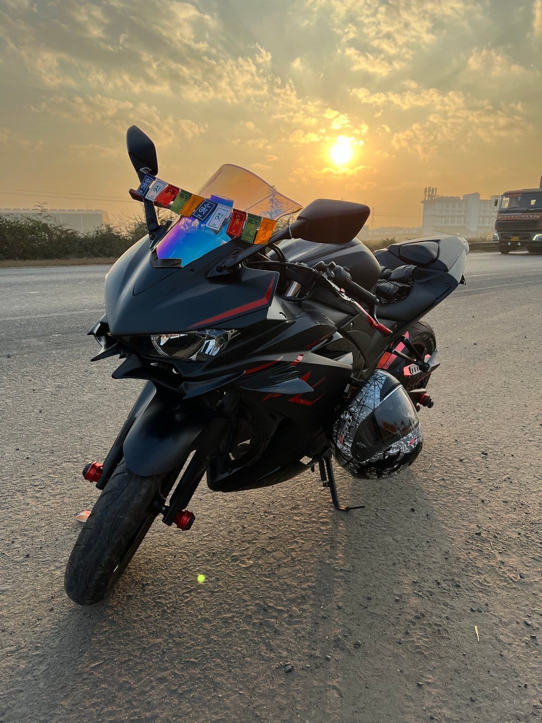Black sportbike with prayer flags and a helmet sits roadside under a glowing golden hour sunset.