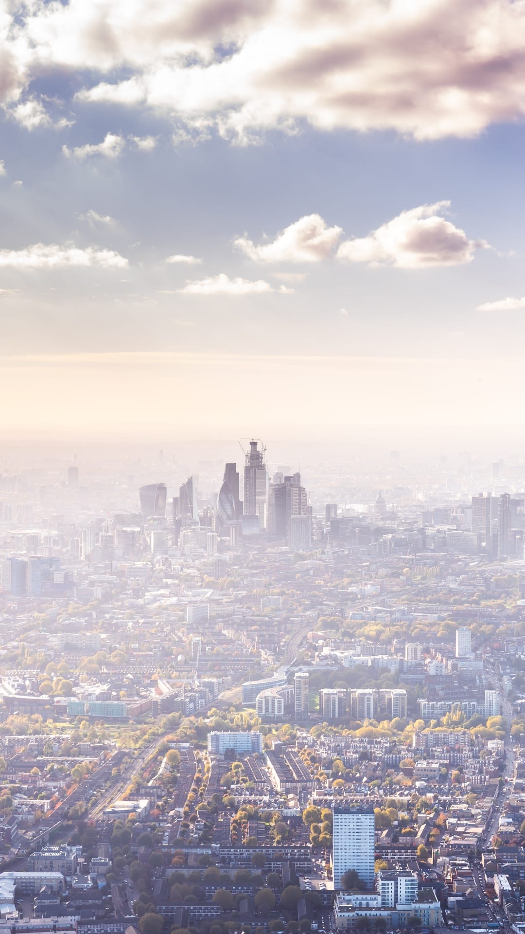 London skyscrapers rise through a thick layer of morning haze above a sprawling grid of residential streets.