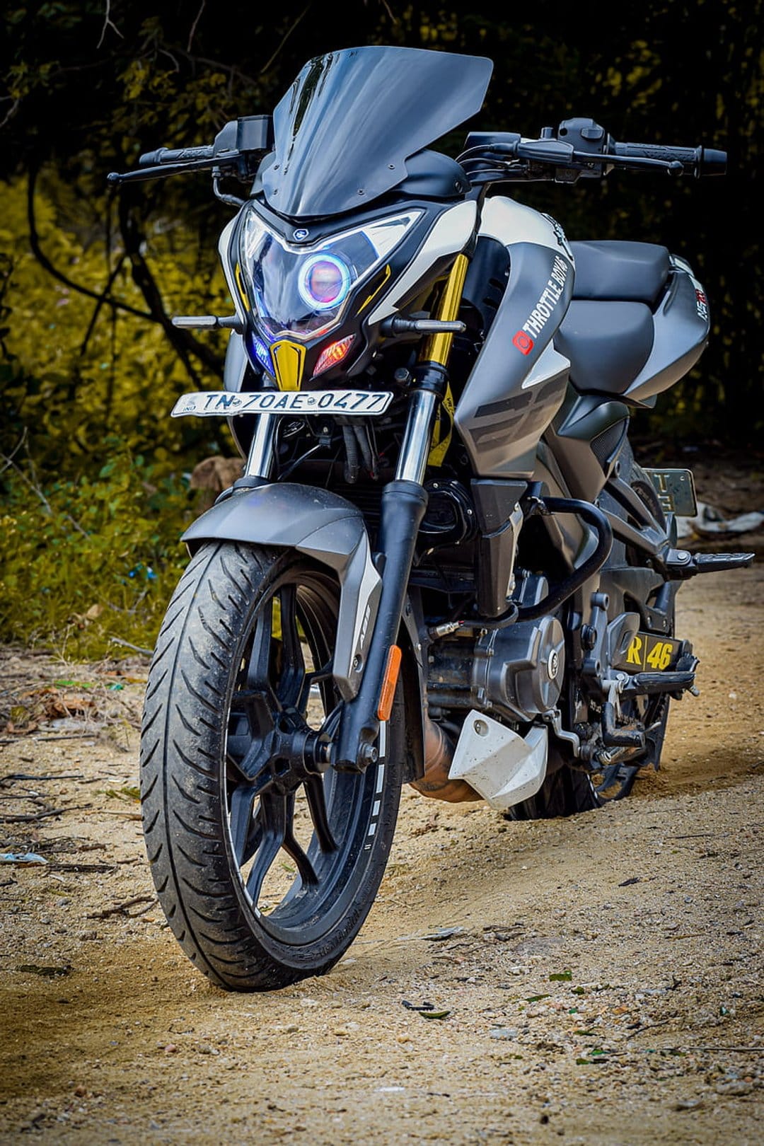 Sportbike with LED halo headlights and yellow accents parked on a rural dirt road surrounded by green plants.