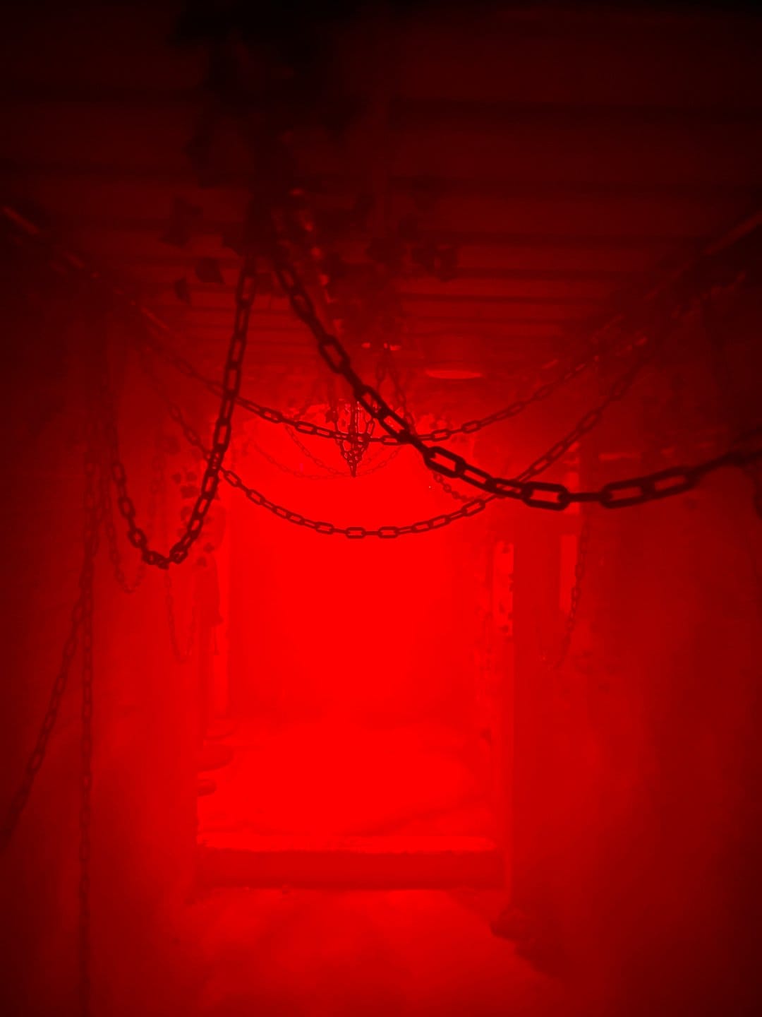 Thick iron chains suspended in a dark room illuminated by a saturated red light with heavy shadows.