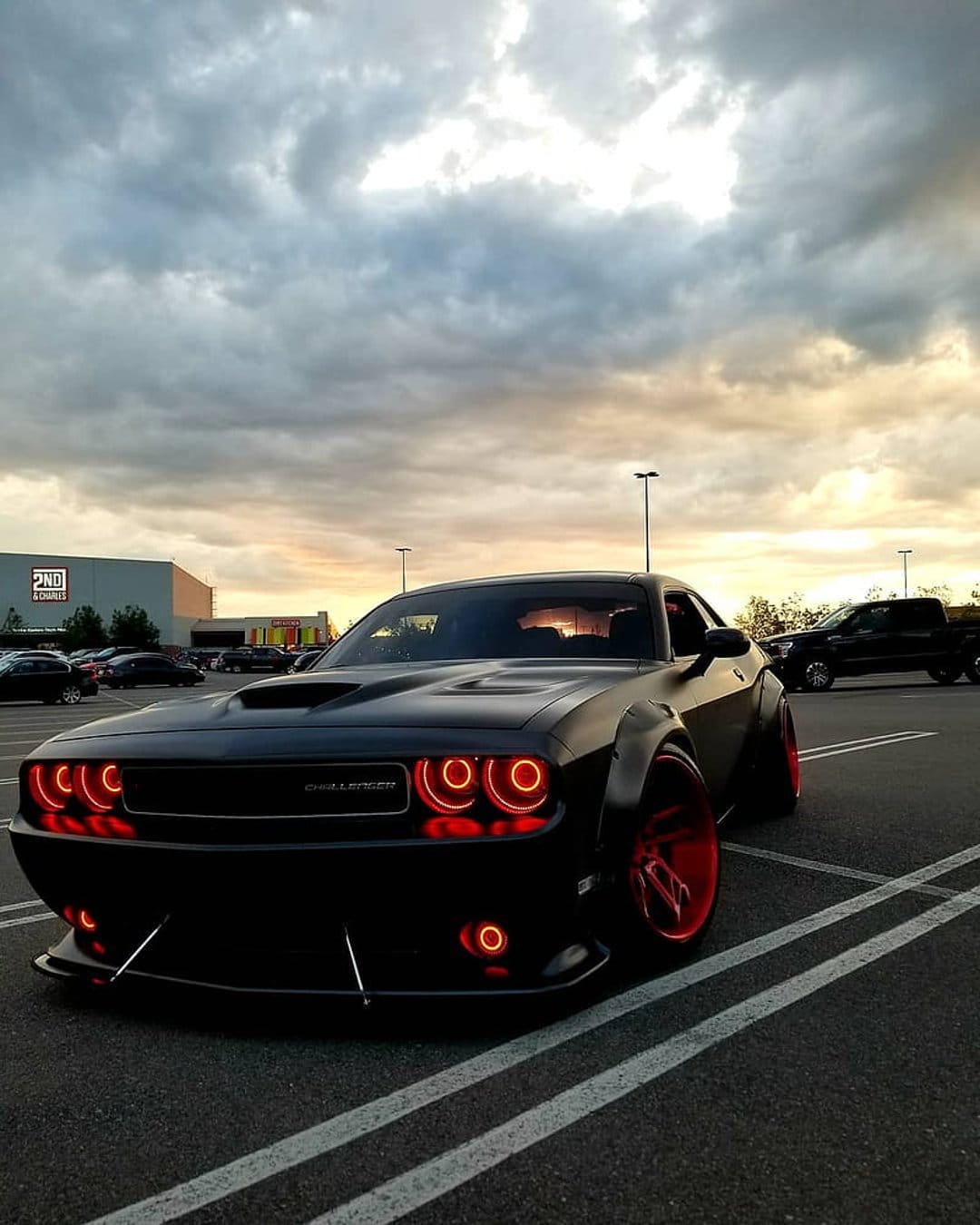 Dodge Challenger widebody with glowing red halo headlights and matching rims parked under a dusky sunset sky.