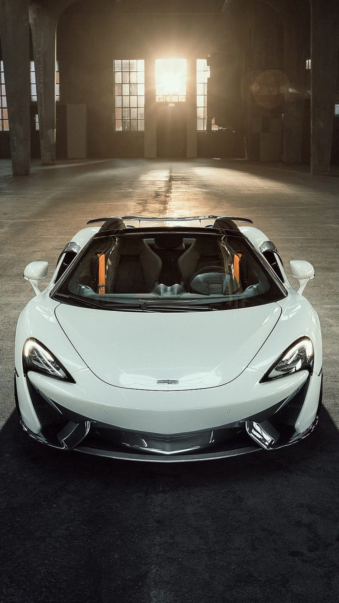 White McLaren convertible parked in a sunlit industrial warehouse with dramatic light through windows.