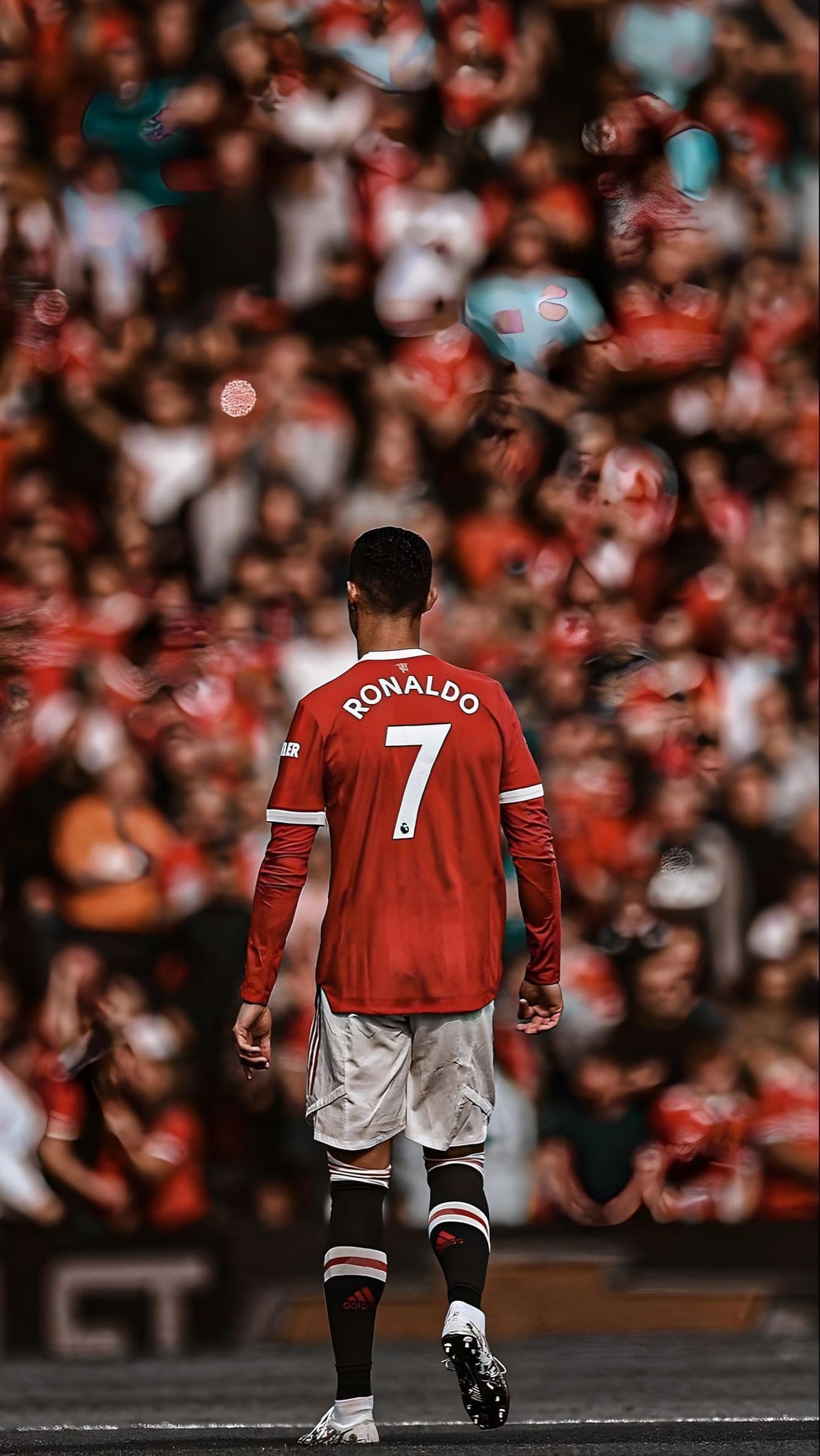 Cristiano Ronaldo in a red Manchester United jersey walks toward a stadium pitch with blurred fans in the background.
