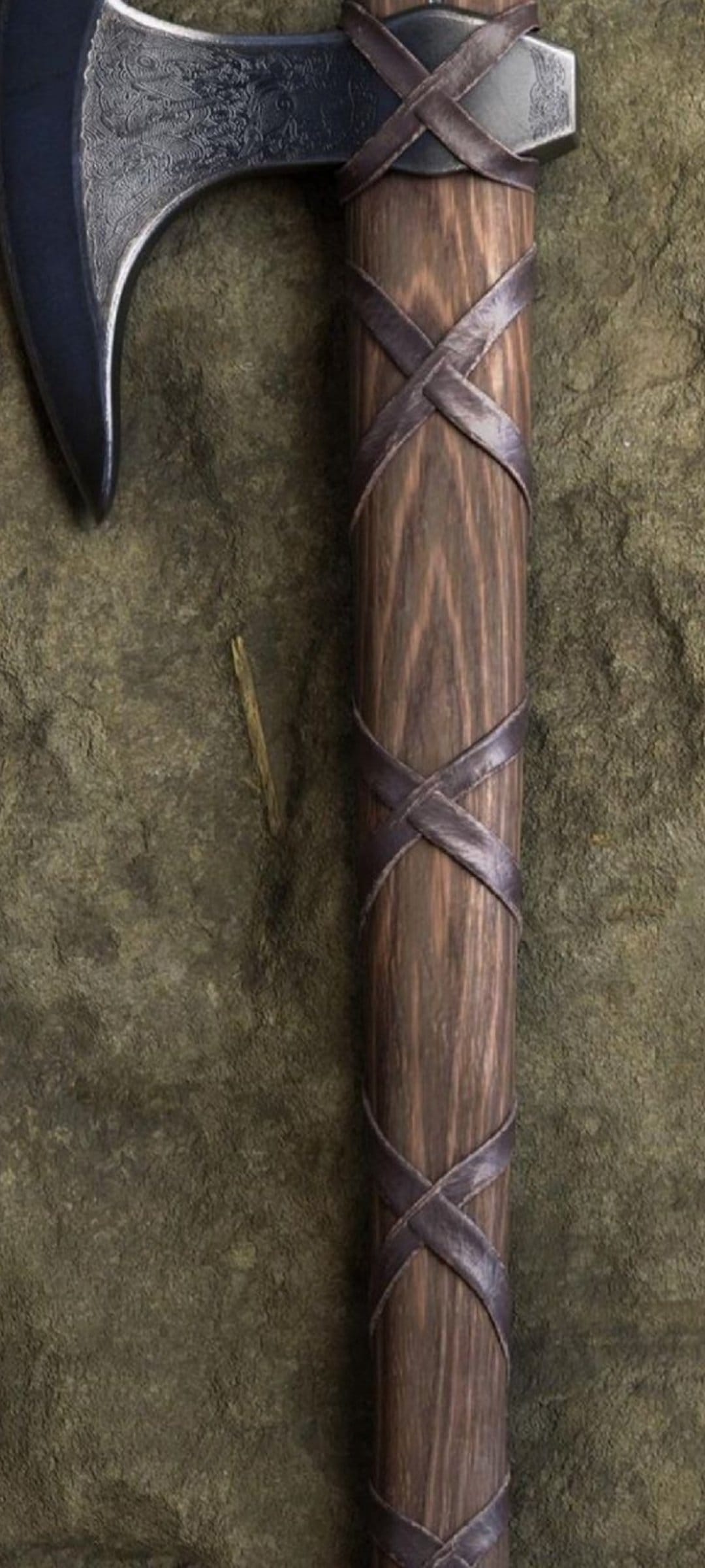Viking battle axe with etched metal blade and criss-cross leather handle straps against an earthy background.
