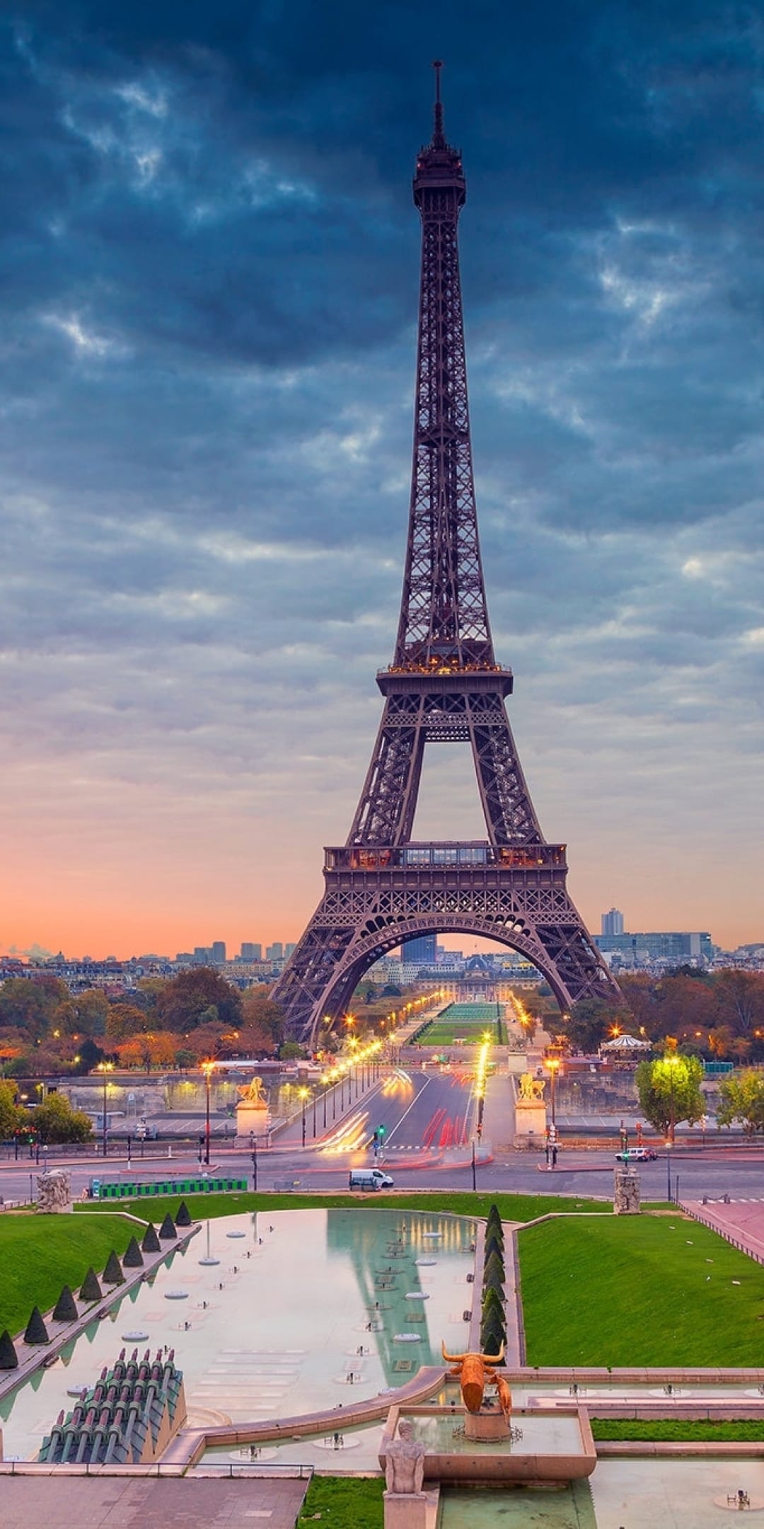 Eiffel Tower illuminated at dusk under a purple and orange sky with glowing city lights and water reflections.