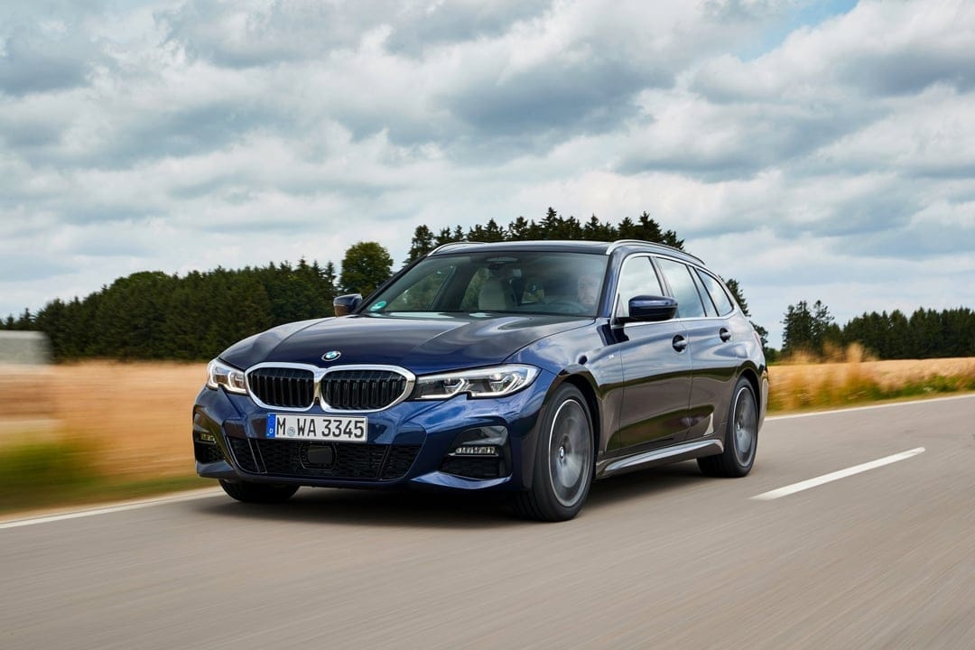 Dark blue BMW sports wagon driving on a road with motion blur, green trees, and a cloudy sky background.