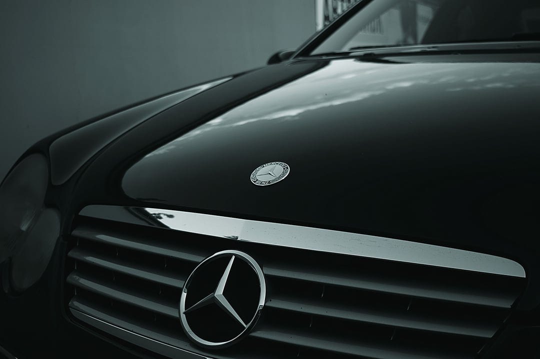Mercedes-Benz three-pointed star emblem and textured grille shown in a monochrome close-up automotive shot.