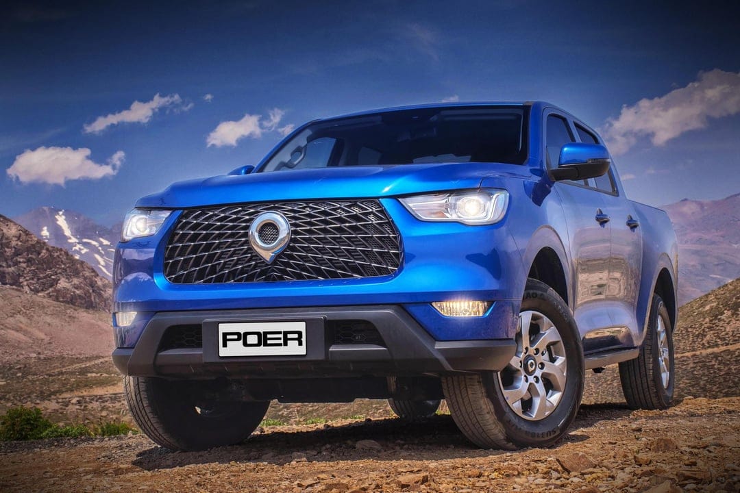 Blue GWM Poer pickup truck on a rocky mountain road under a bright sky with rugged peaks in the background.