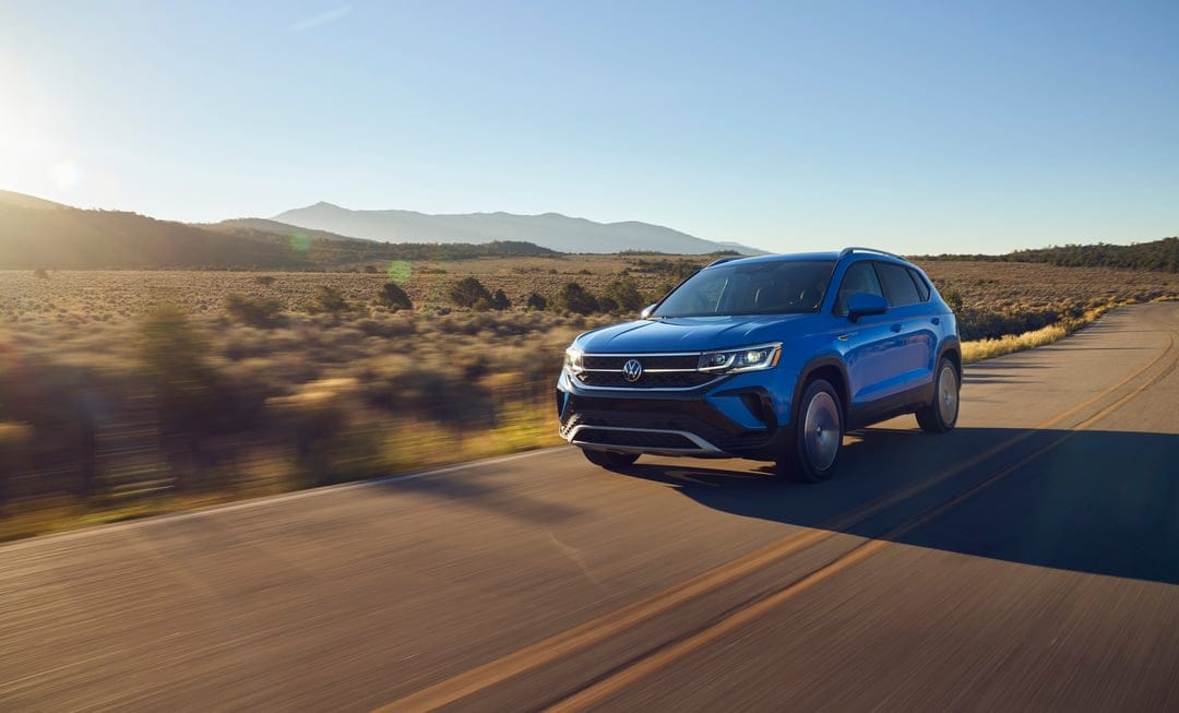 Blue Volkswagen SUV driving on a desert road with golden hour lighting and distant mountains in landscape view.