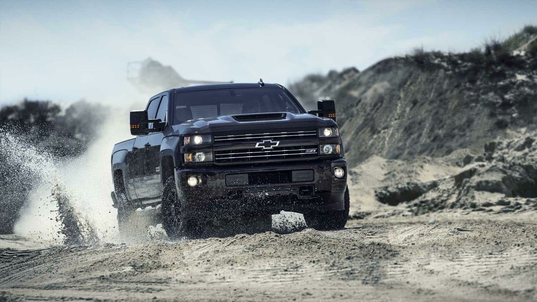 Black Chevrolet Silverado Z71 pickup truck splashing through sand and water in a rugged outdoor quarry.