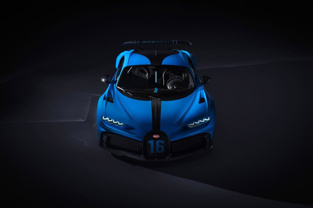 Blue Bugatti Chiron Pur Sport hypercar front view with glowing LED headlights on a black studio background.