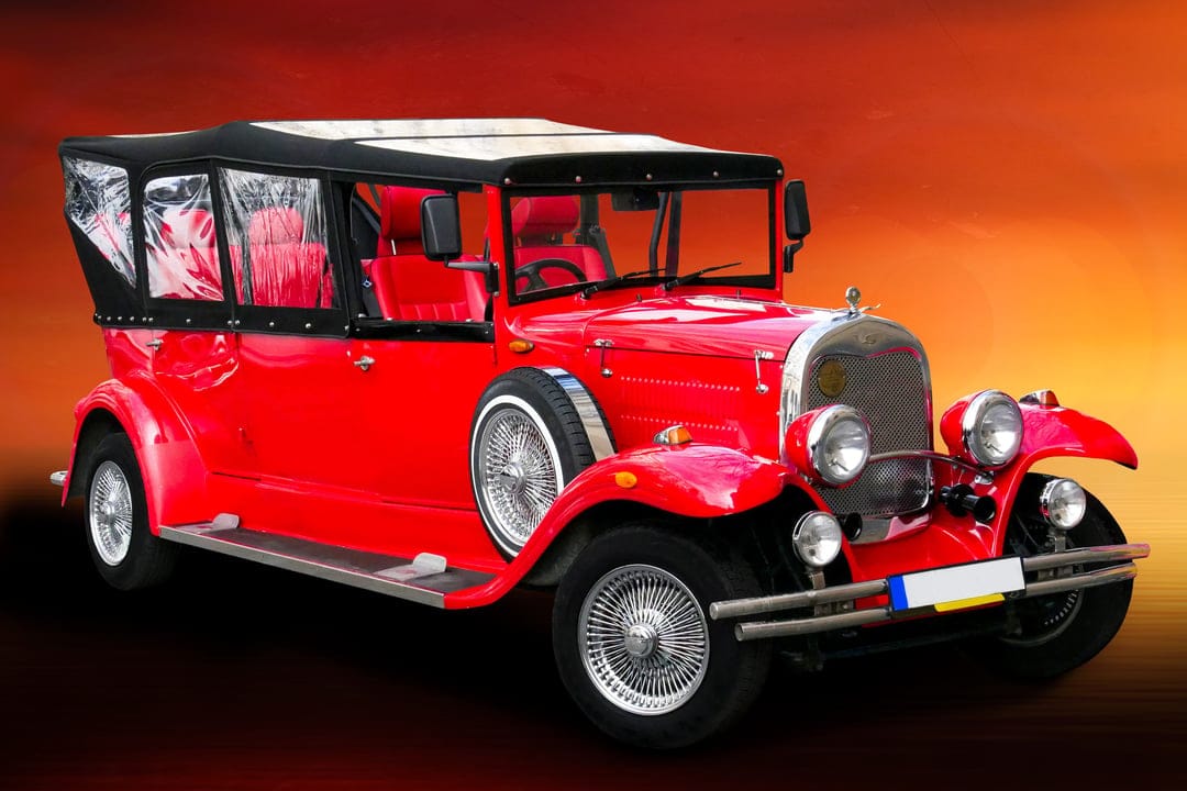 Red vintage convertible car with spoked wheels and chrome trim against a warm orange and yellow gradient background.