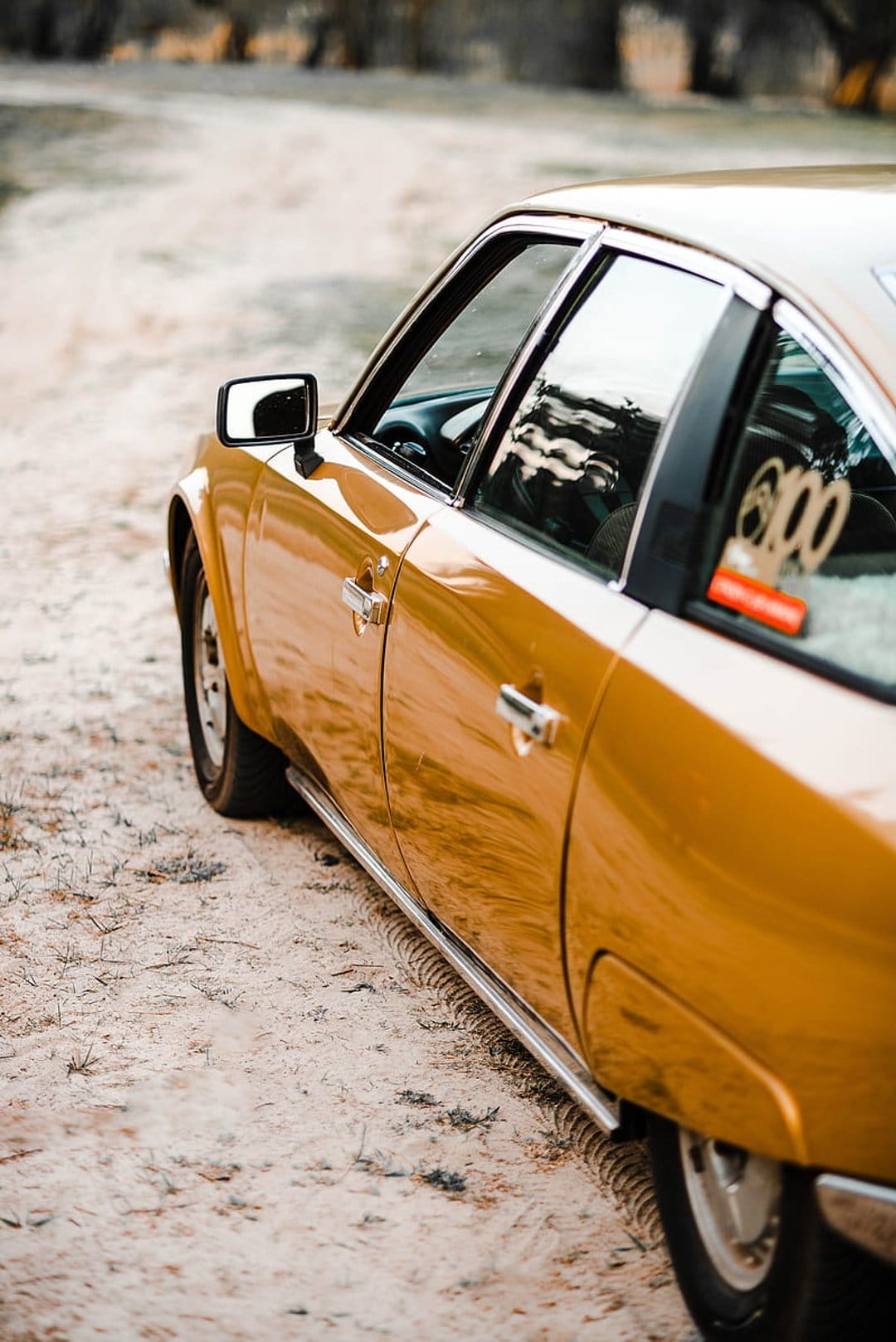 Golden Citroën CX parked on a sandy path with chrome accents and sky reflections in a low-angle shot.