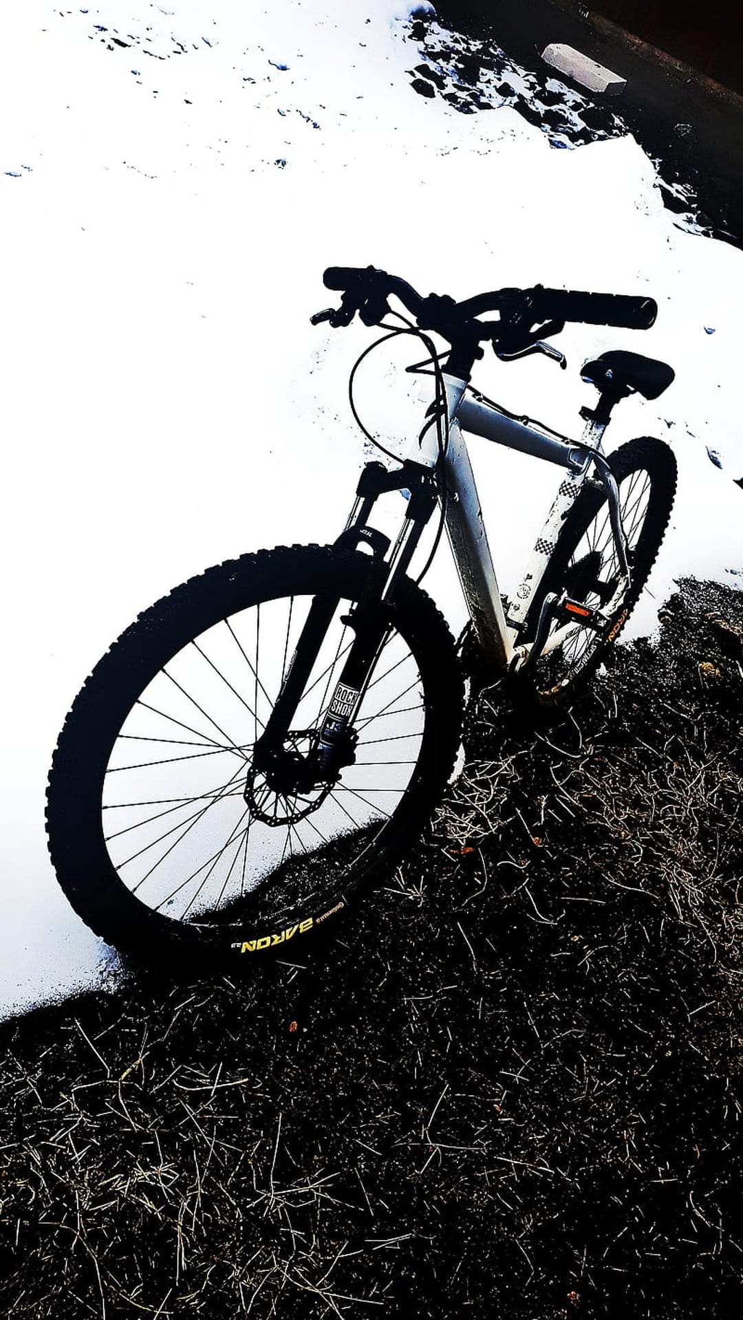 Mountain bike silhouette against a bright white snowy field with dark winter grass in the foreground.