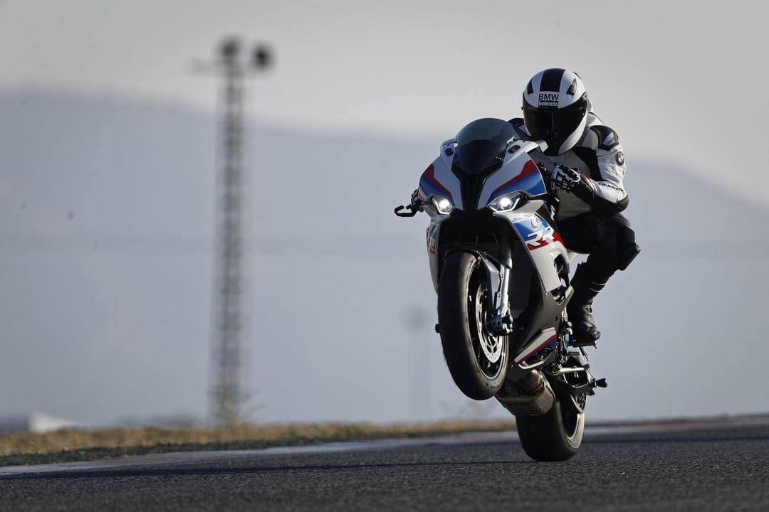BMW S1000RR motorcycle performing a front wheelie on a racetrack with a rider in white racing leathers.