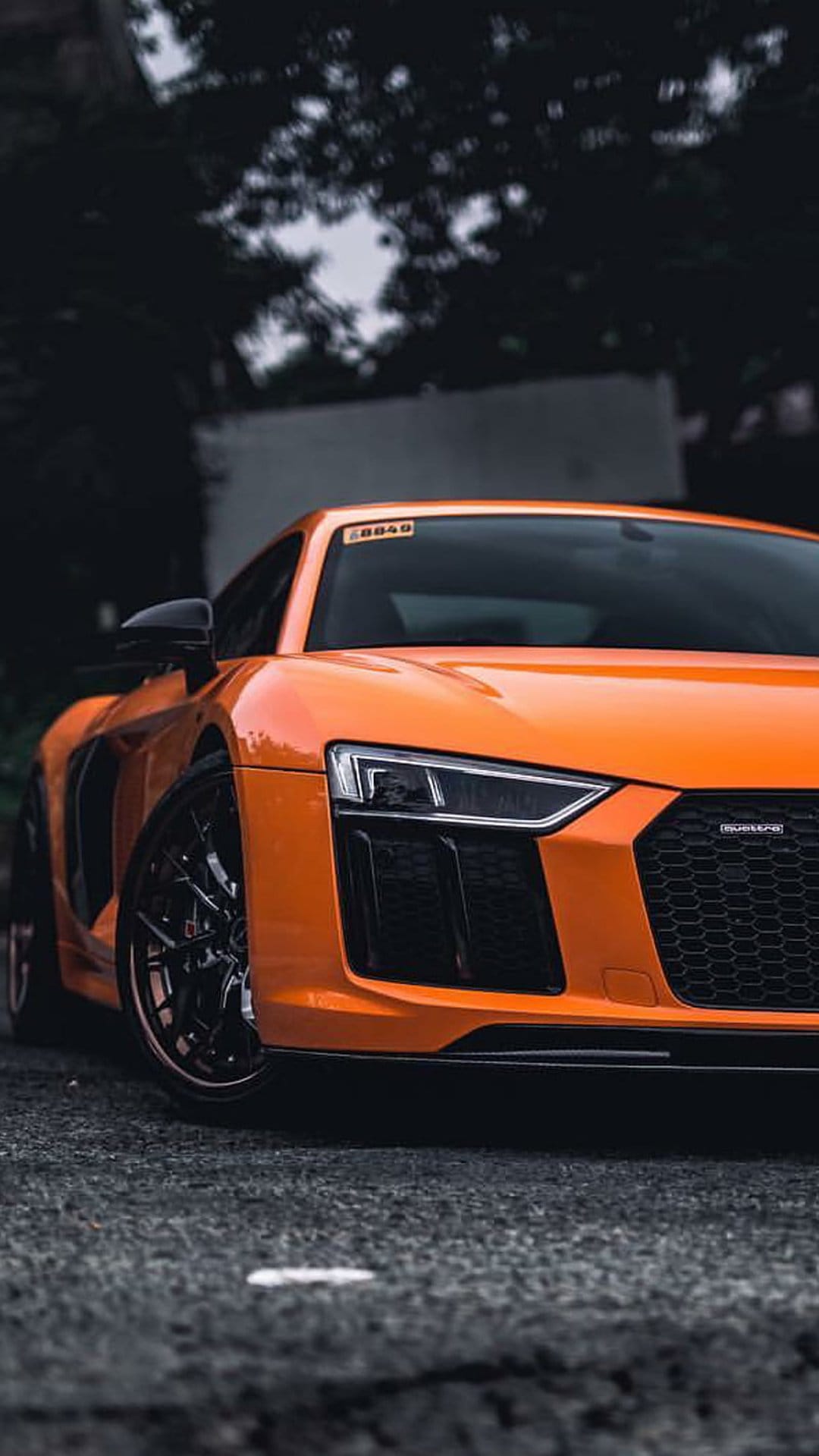 Orange Audi R8 features aggressive front grilles and LED headlights parked on a dark asphalt road surface.