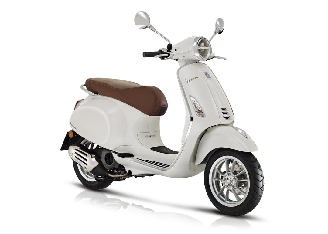 White Vespa Primavera scooter with a brown leather seat and chrome accents on a seamless white studio background.