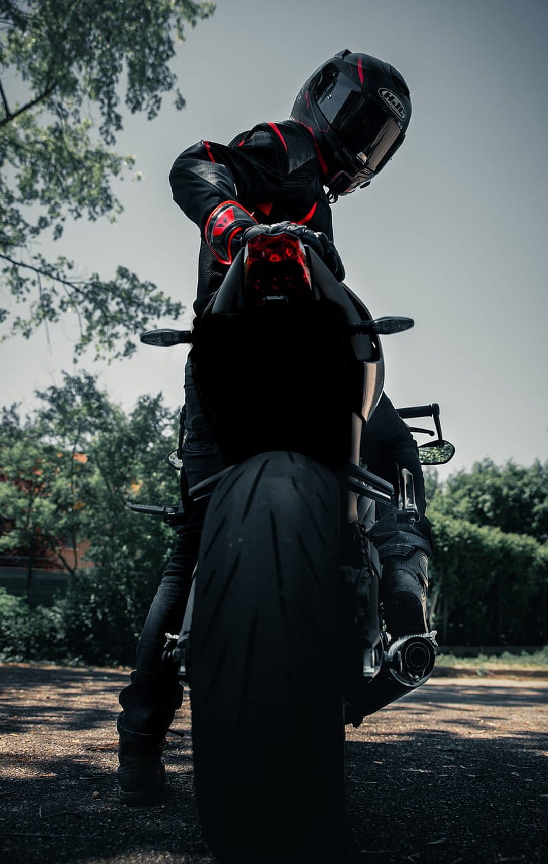 Motorcyclist in a red and black suit sits on a sportbike with a large rear tire and illuminated tail light.