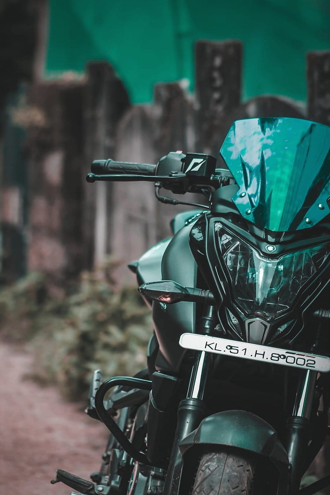 Black motorcycle front view with a blue tinted windshield, chrome handlebars, and a glowing round headlight.