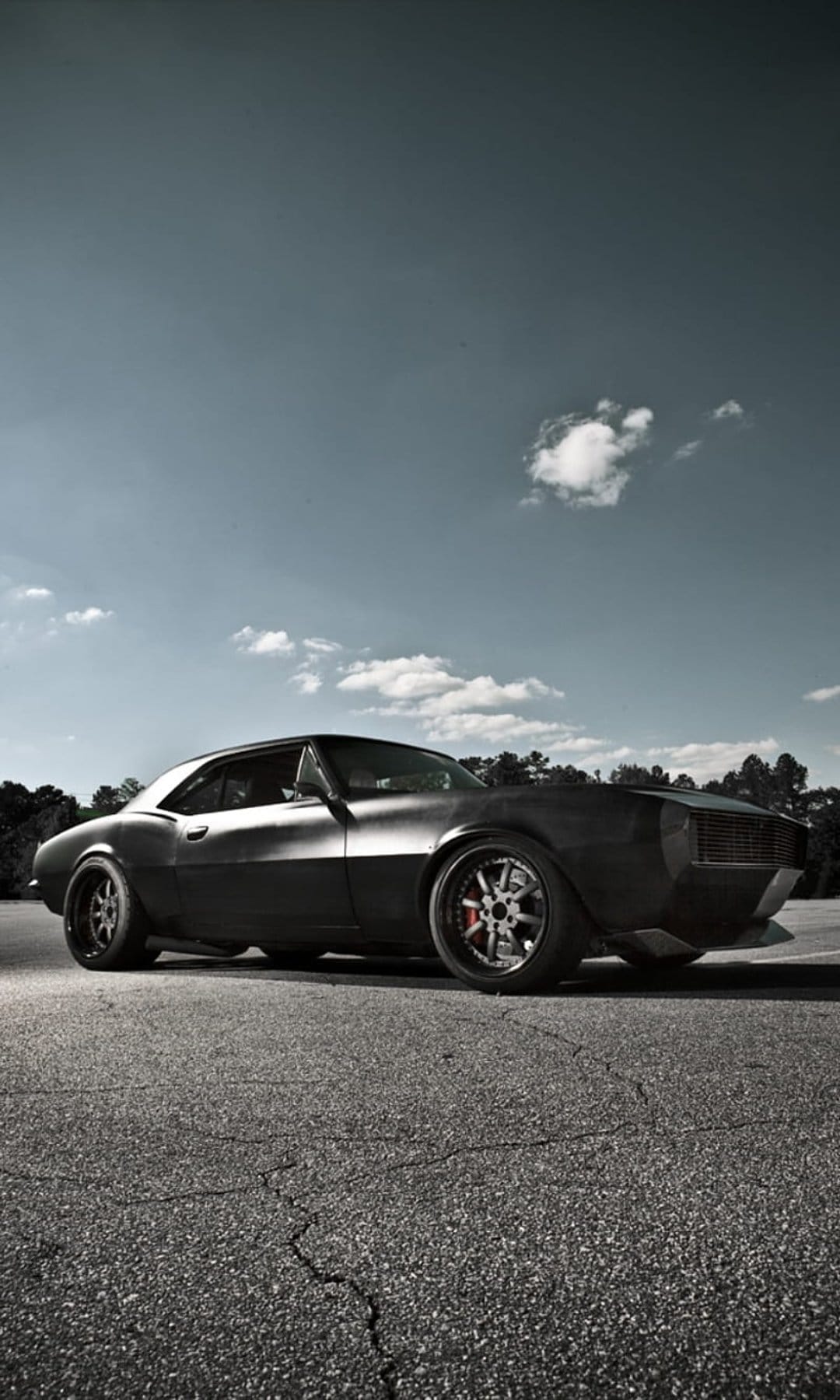 Matte black Chevrolet Camaro restomod on cracked asphalt under a cloudy sky with visible custom brake calipers.
