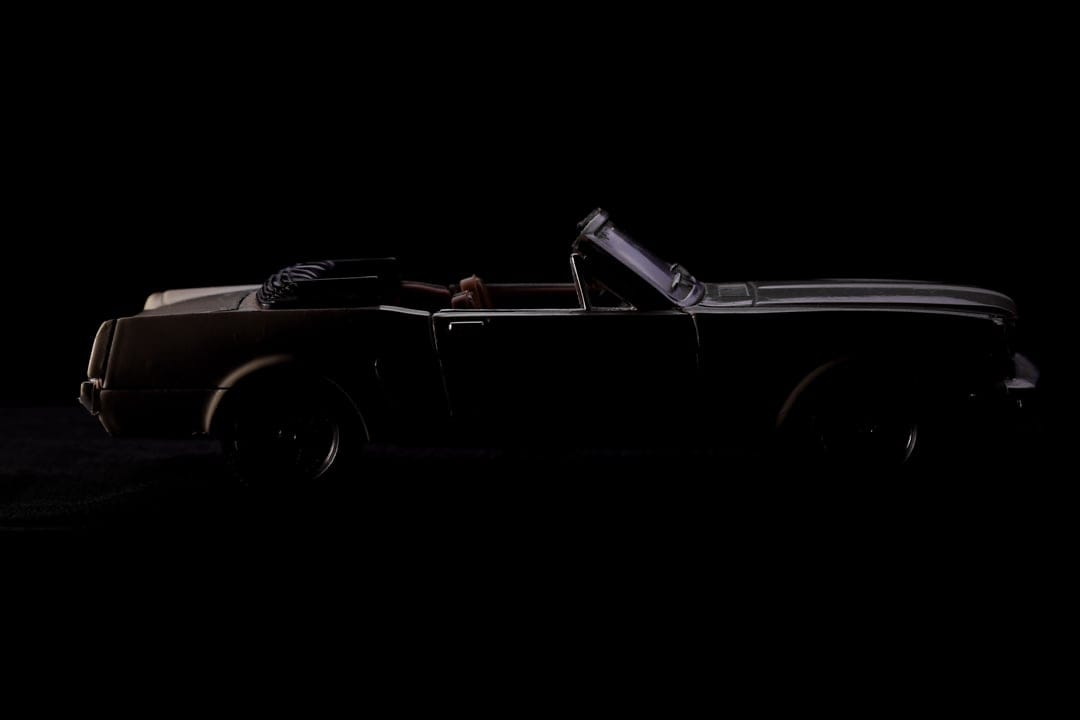 Vintage convertible car silhouette with rim lighting against a black background for mobile phone screens.