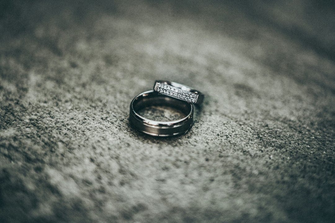 Two silver wedding rings, one featuring small diamonds, rest on a grey textured surface with macro focus.