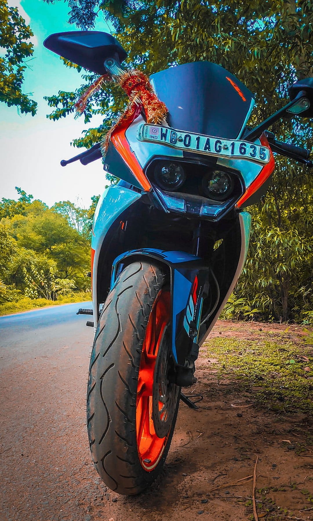 KTM RC motorcycle with orange and blue accents parked on a dusty forest road surrounded by green trees.