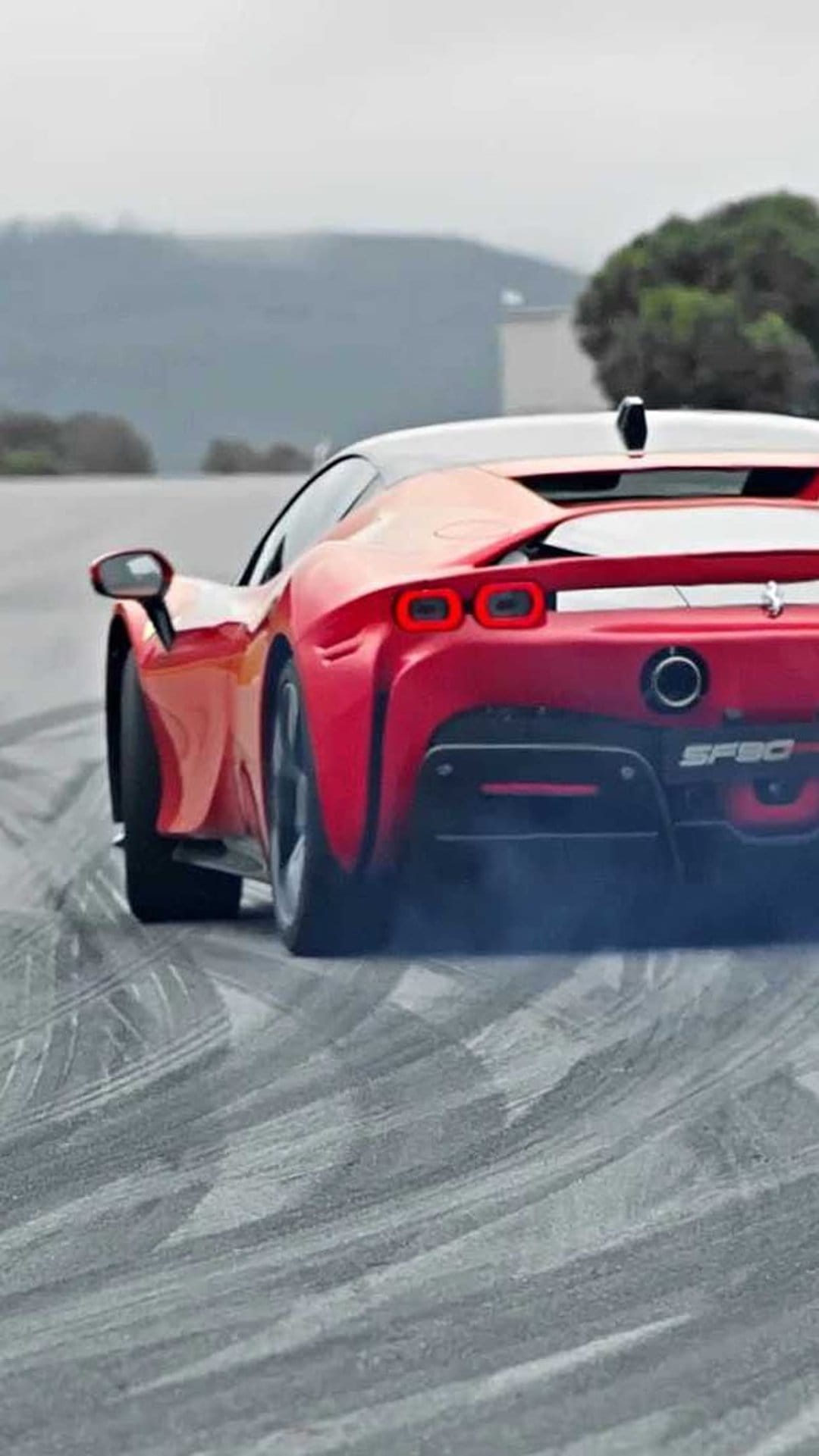 Ferrari SF90 supercar performing a rear tire burnout with thick white smoke on a textured grey asphalt surface.