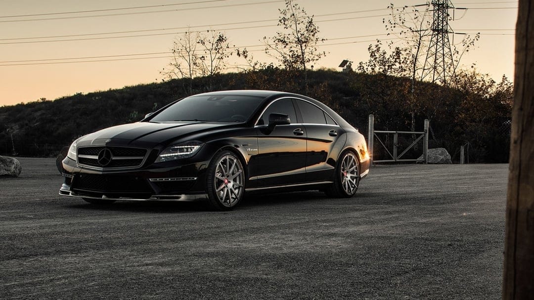 Black Mercedes-Benz CLS 63 AMG parked on a gravel lot during sunset with golden reflections on the body.