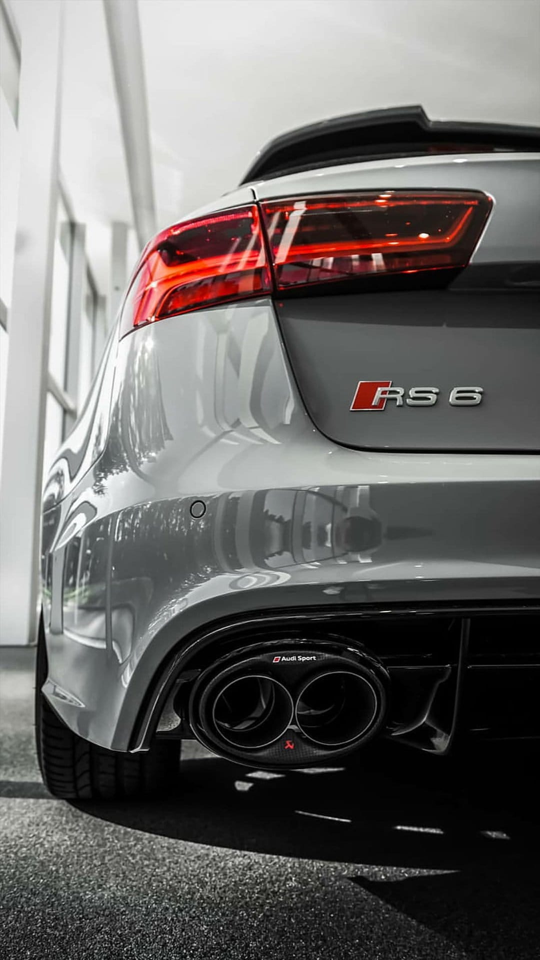 Audi RS 6 rear view featuring silver metallic paint, glowing LED taillights, and black quad exhaust outlets.