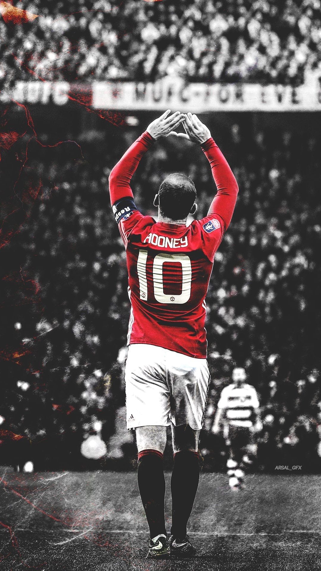 Wayne Rooney in a red jersey raises his arms in celebration against a black and white stadium crowd.