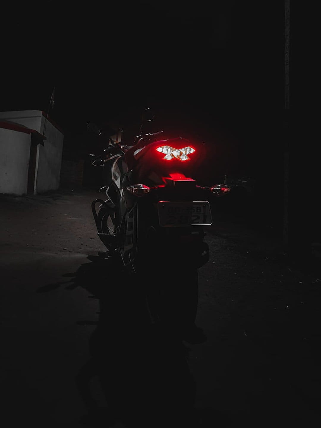 Red motorcycle tail lights glowing intensely in a dark night environment with subtle reflections on the bike.