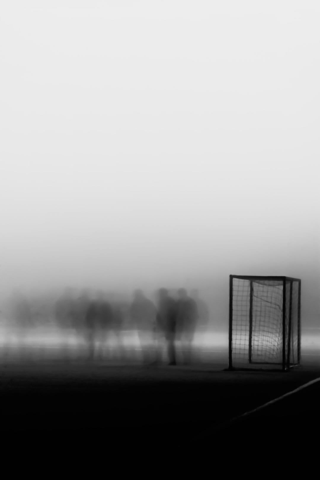 Soccer goal on a misty beach with blurred silhouettes of people walking in the distance under a foggy sky.