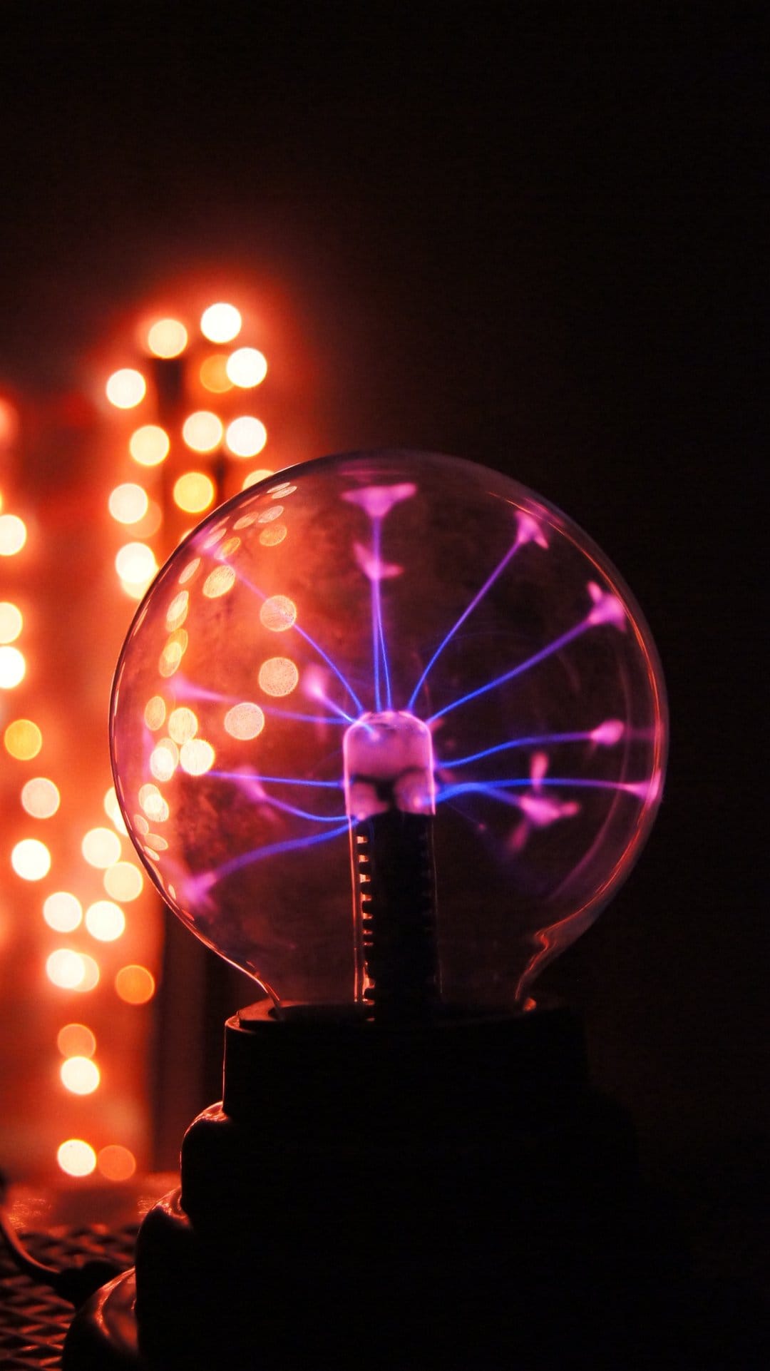 Plasma ball emitting blue electrical discharges in front of blurred orange bokeh lights on a dark background.