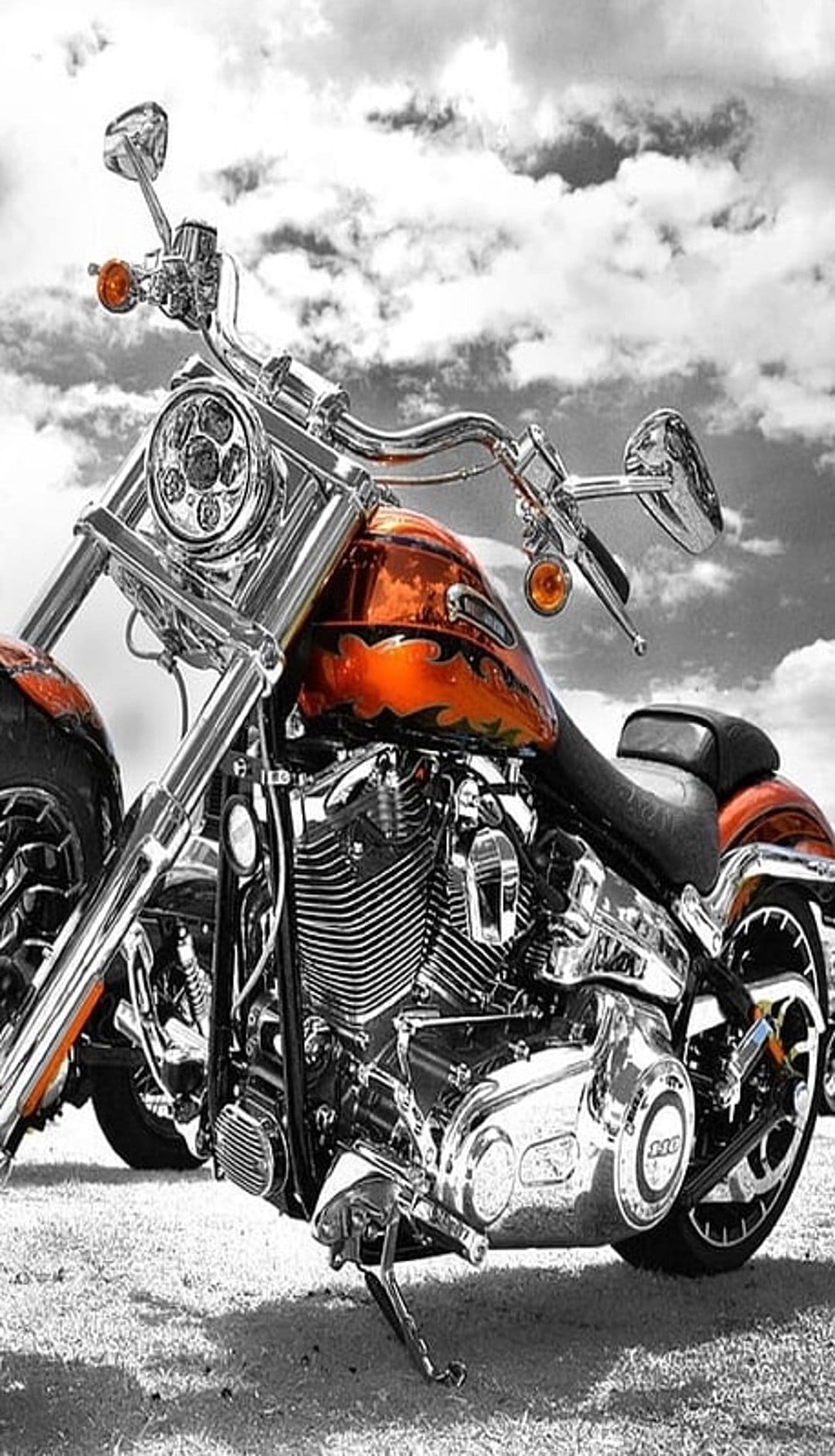 Custom Harley Davidson motorcycle with orange flame graphics and chrome engine parts against a cloudy sky.