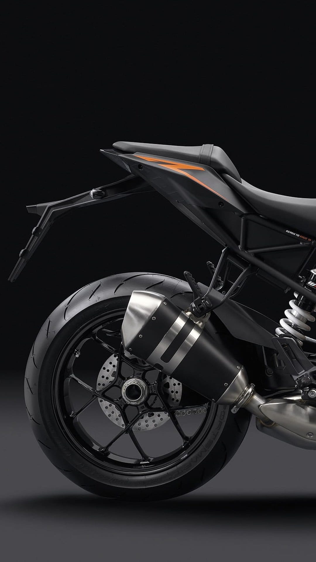 KTM motorcycle rear wheel featuring a perforated brake disc and a sleek black exhaust with orange tail accents.