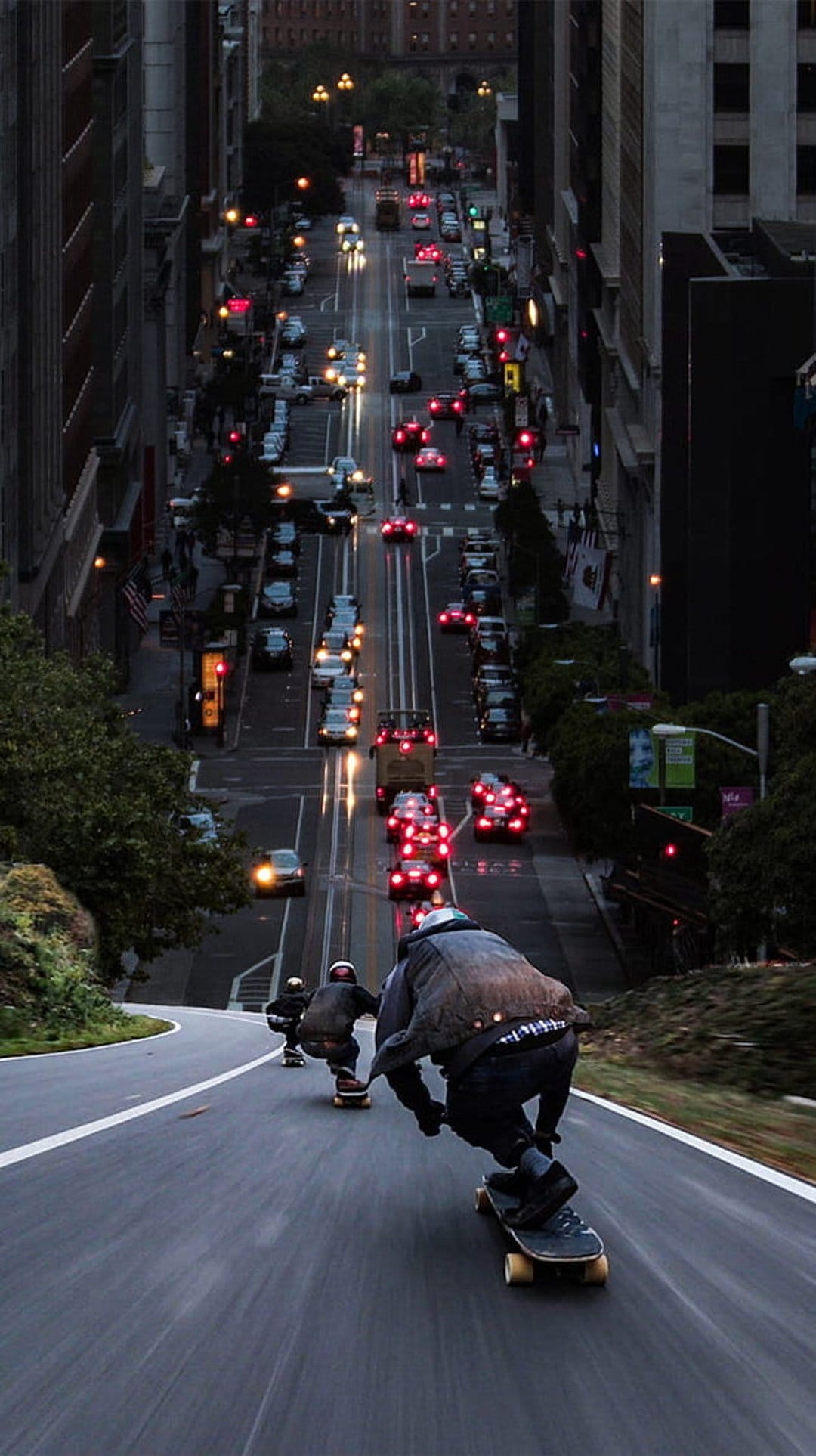 Three longboarders in safety gear descend a steep San Francisco hill as car lights blur into glowing streaks.