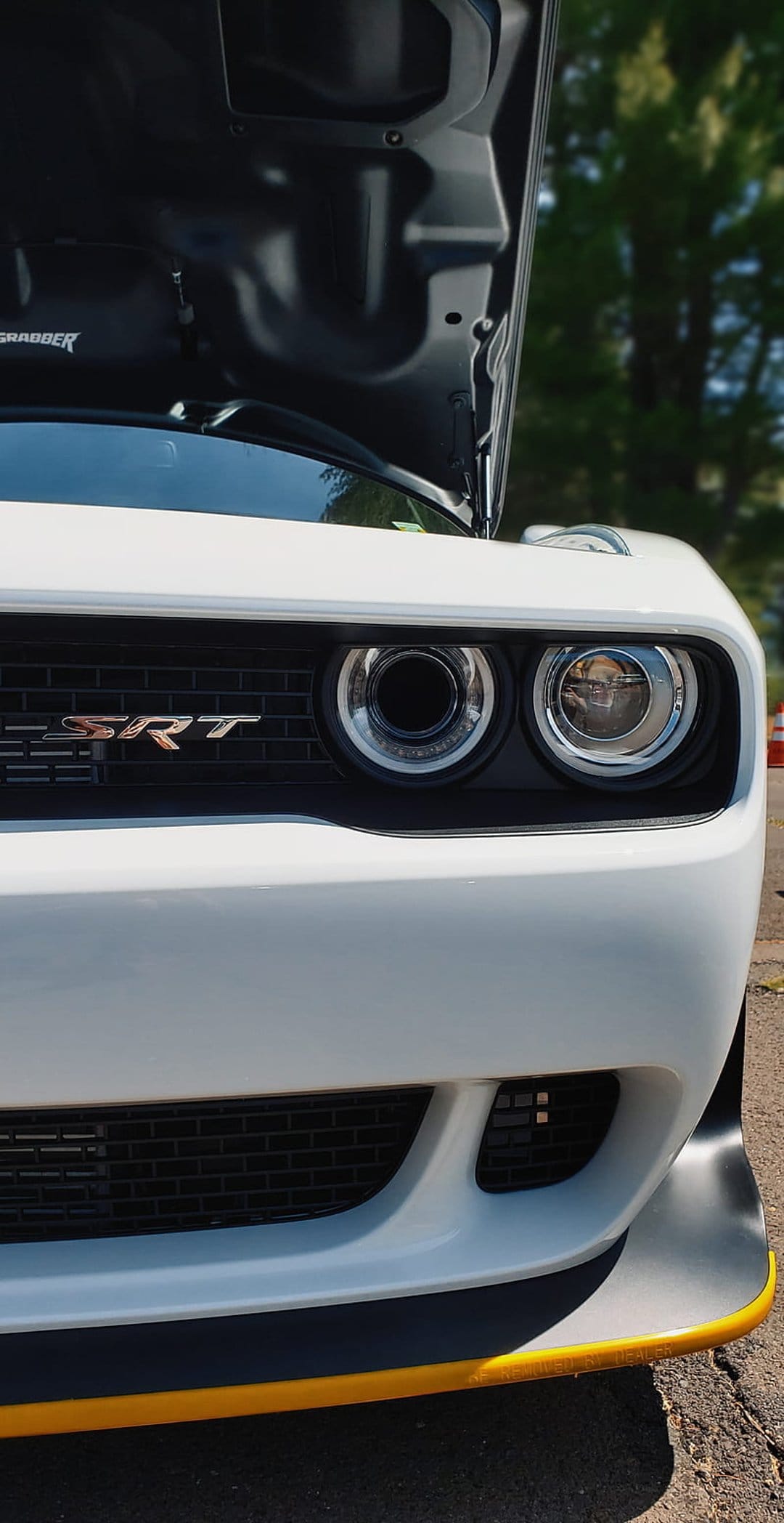 White Dodge Challenger SRT with an open hood, yellow front splitter trim, and exposed engine components.