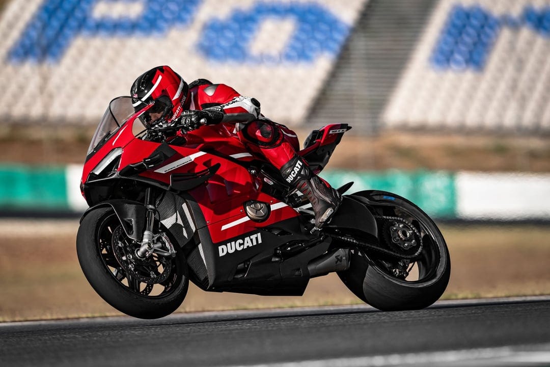 Red Ducati Superleggera V4 motorcycle racing on a track with a rider in red leathers leaning into a turn.