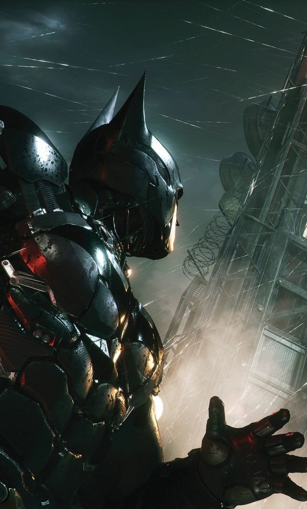 Batman in armored tactical suit stands in rain next to industrial tower with red and white lighting accents.