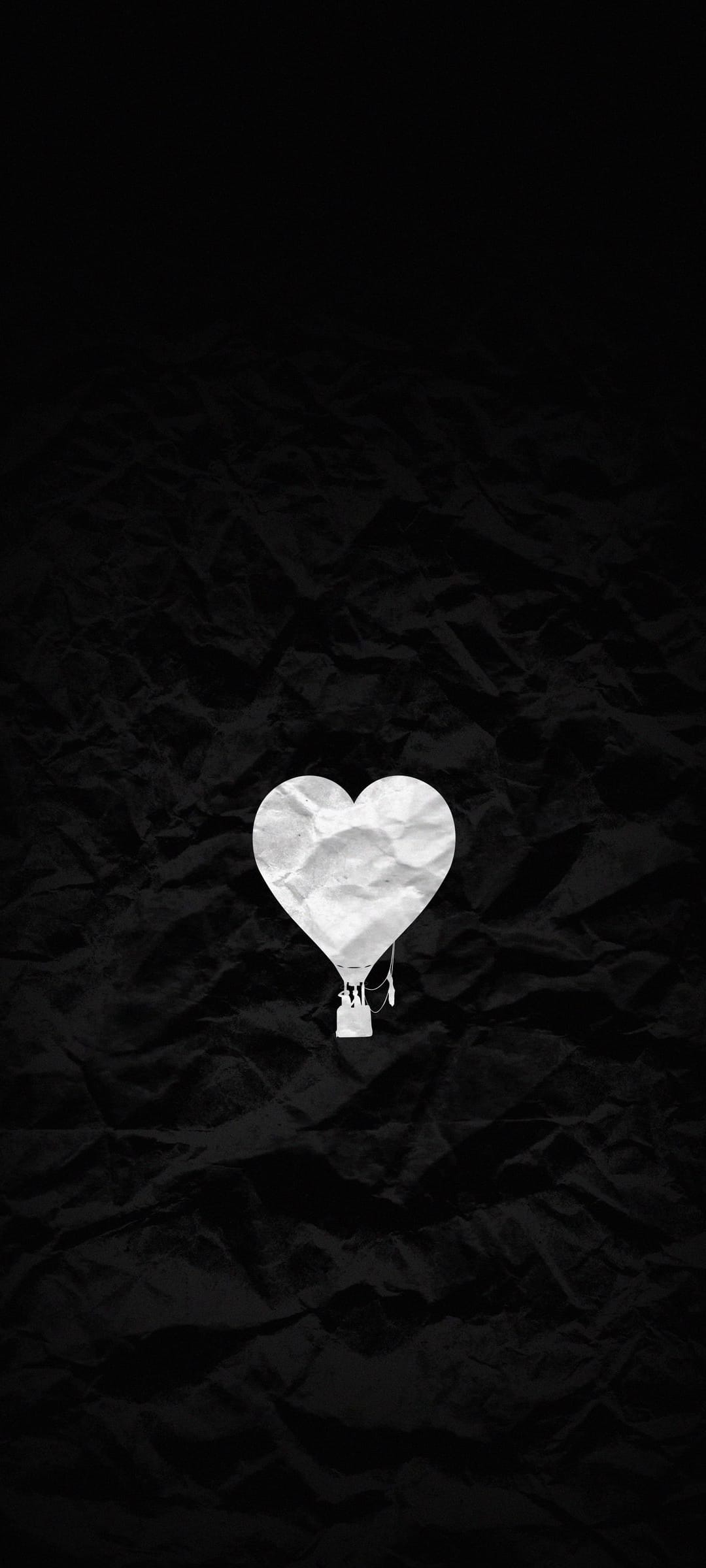 White crumpled paper heart shaped like a hot air balloon floating against a solid black textured background.