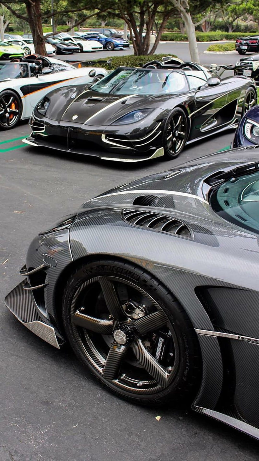 Carbon fiber supercars with detailed weave patterns parked in a row at an outdoor automotive exhibition.