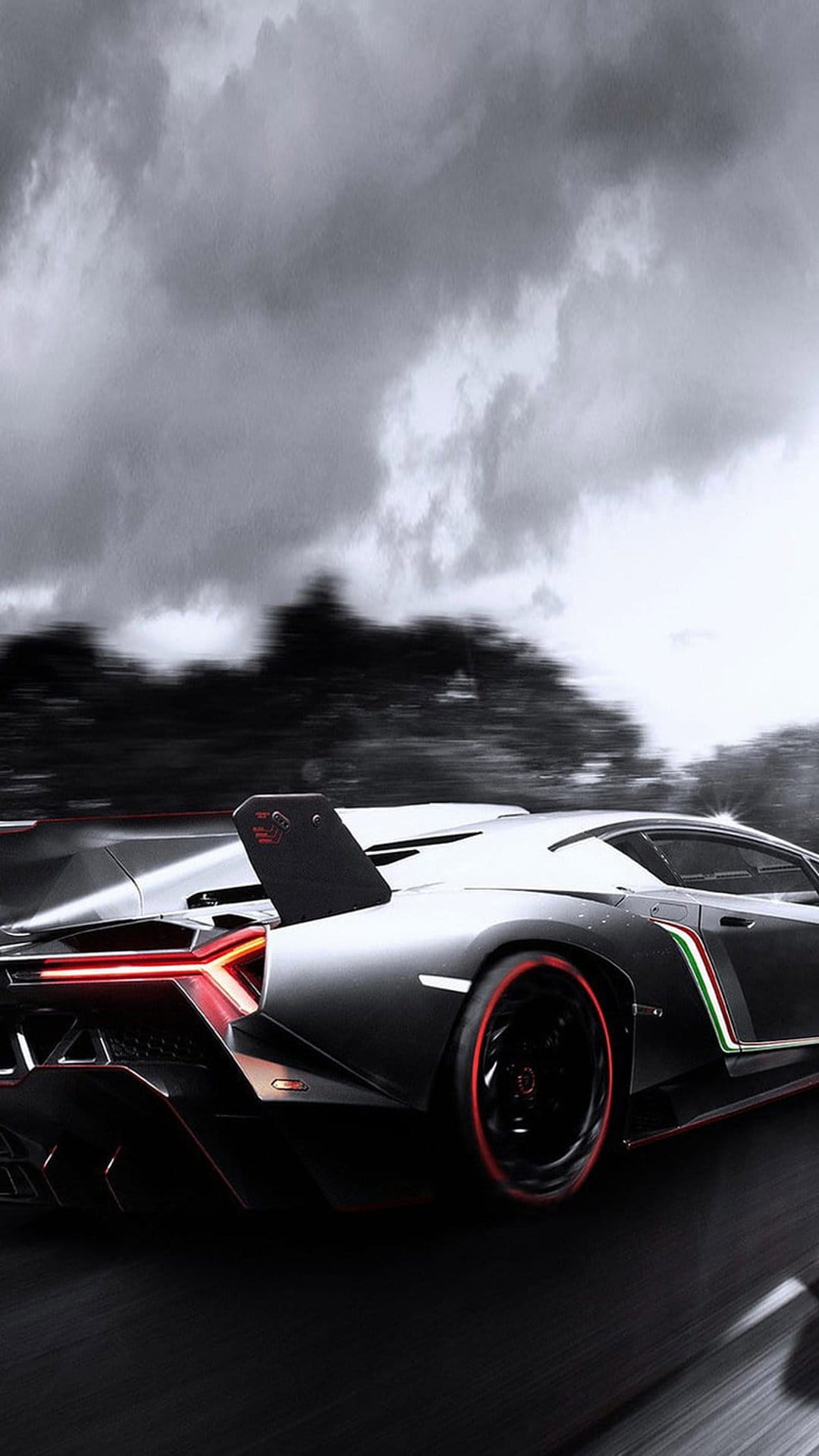 Lamborghini Veneno rear view with red accents and a large wing on a dark wet road under a stormy grey sky.