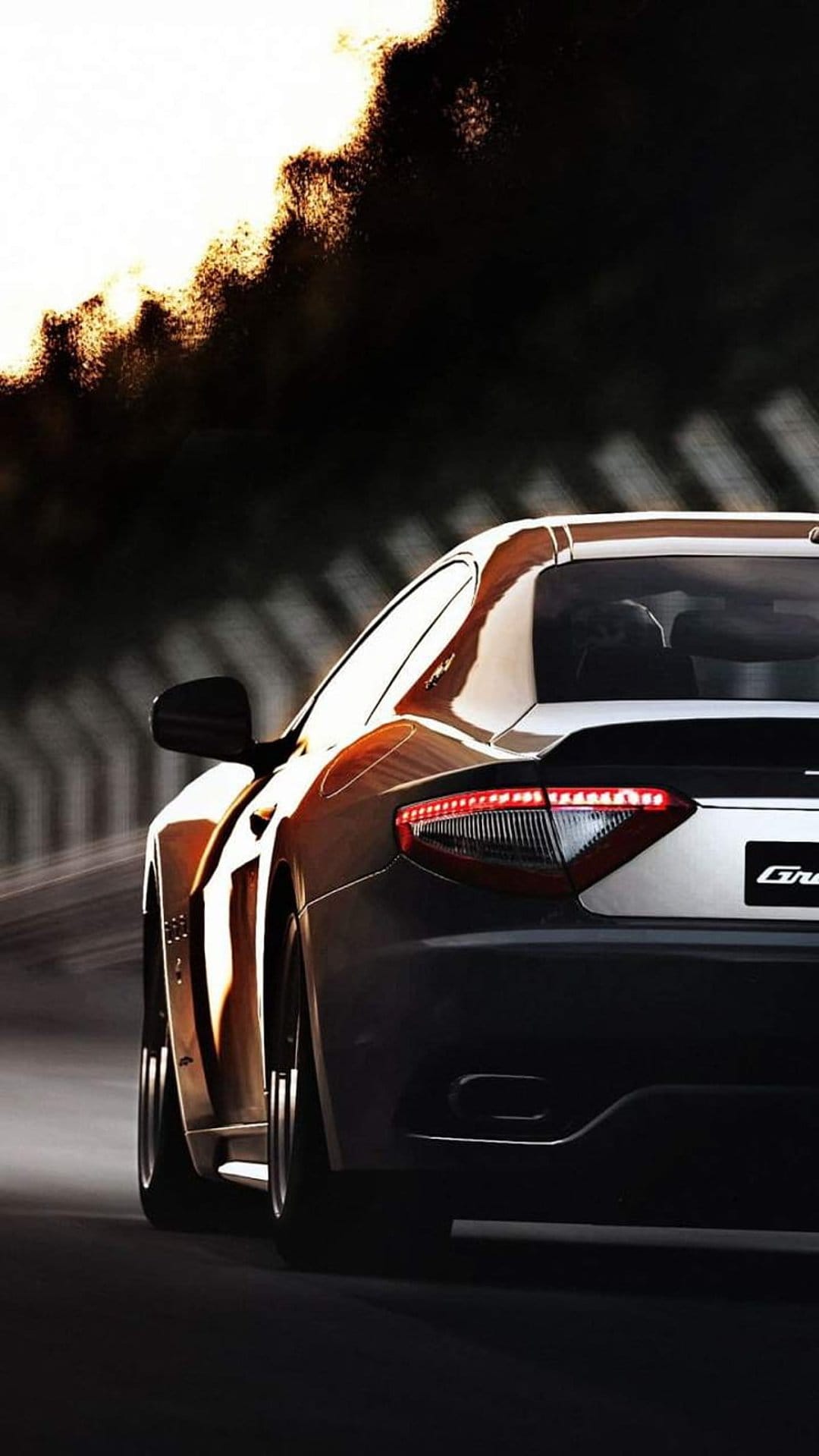 Maserati GranTurismo rear view with red glowing taillights and motion blur on a dark asphalt road at night.