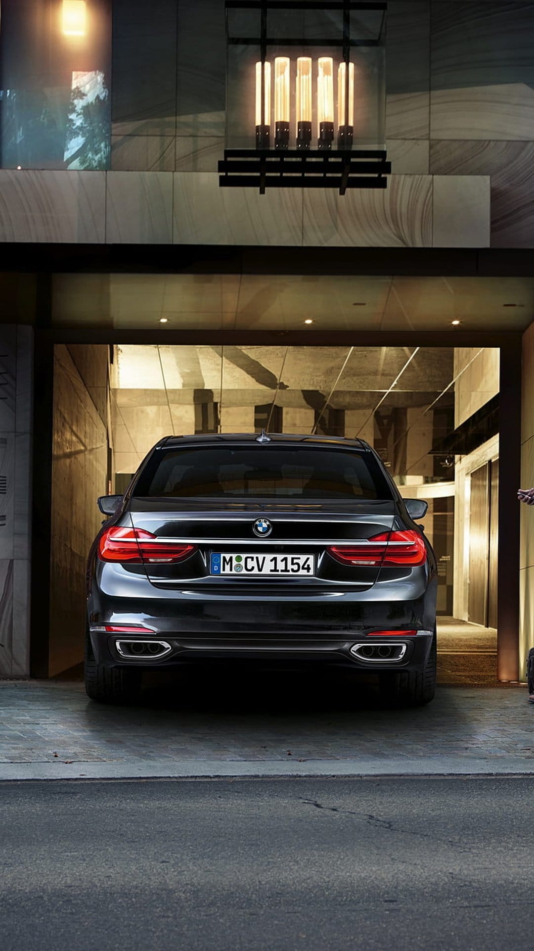 Black BMW sedan parked on a marble driveway at night with warm lights reflecting on the car's polished surface.
