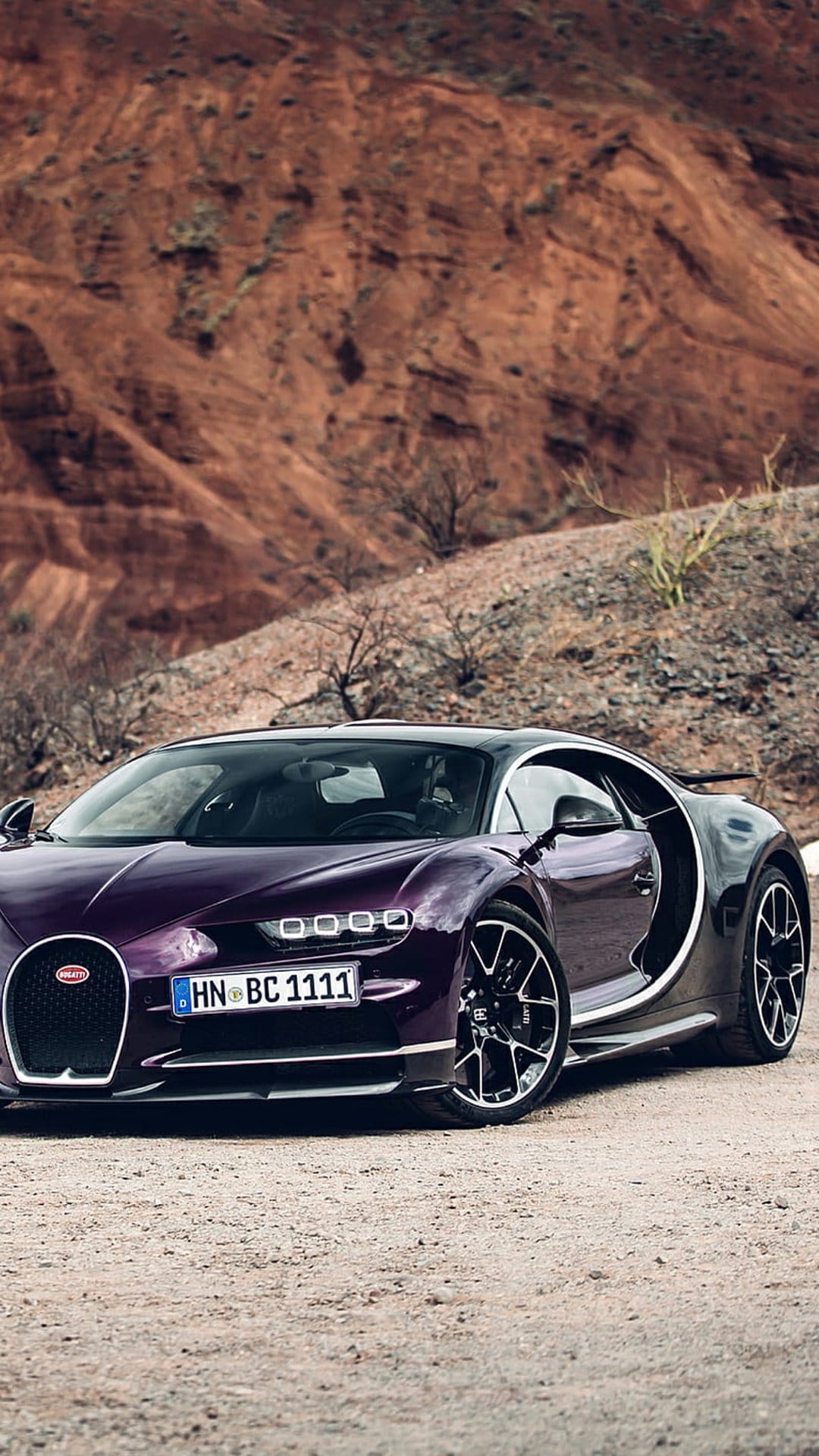 Purple Bugatti Chiron hypercar parked on a dry desert road with rocky mountains and sand in the background.