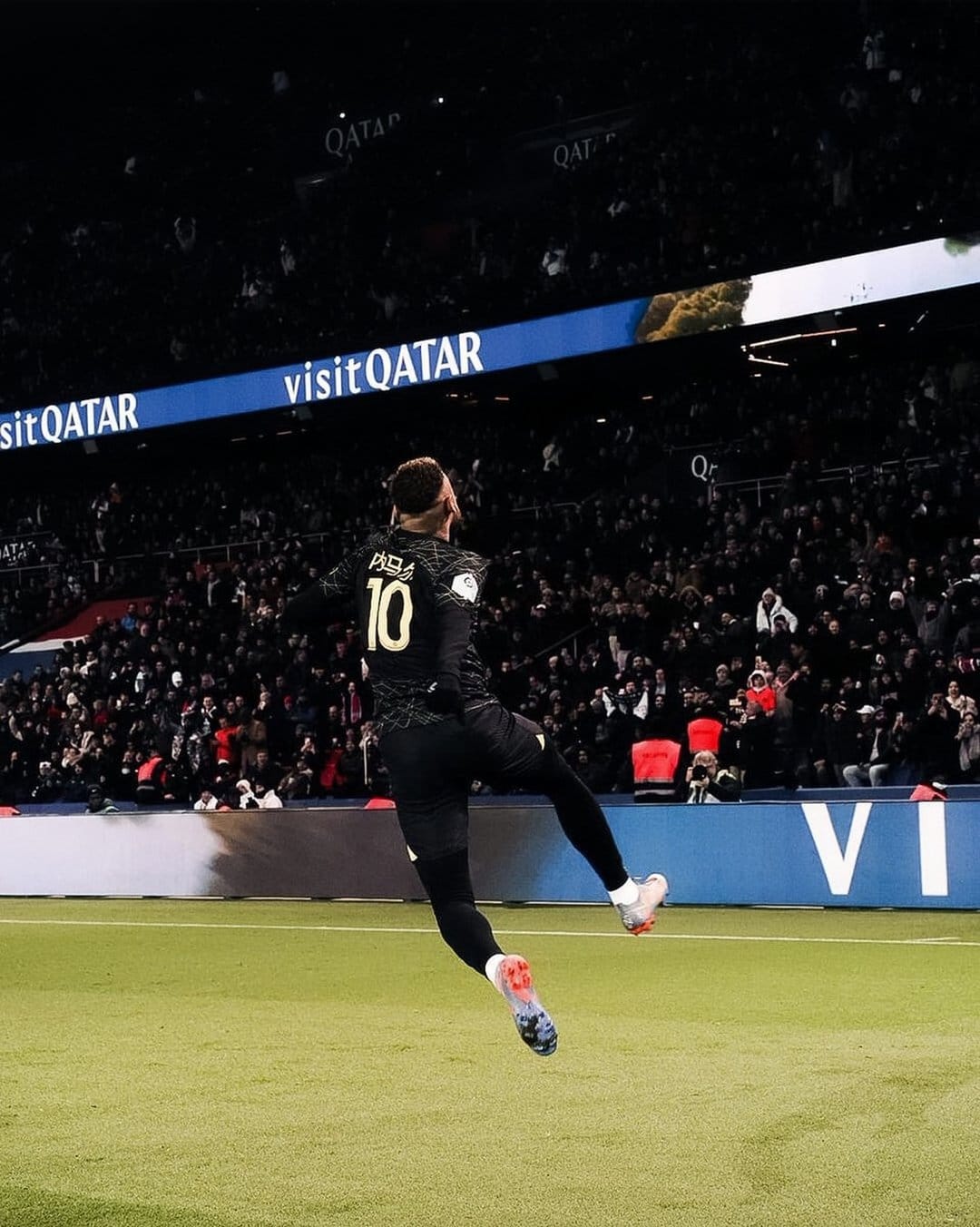Kylian Mbappé leaps during celebration at Parc des Princes stadium with blurred spectators in the background.