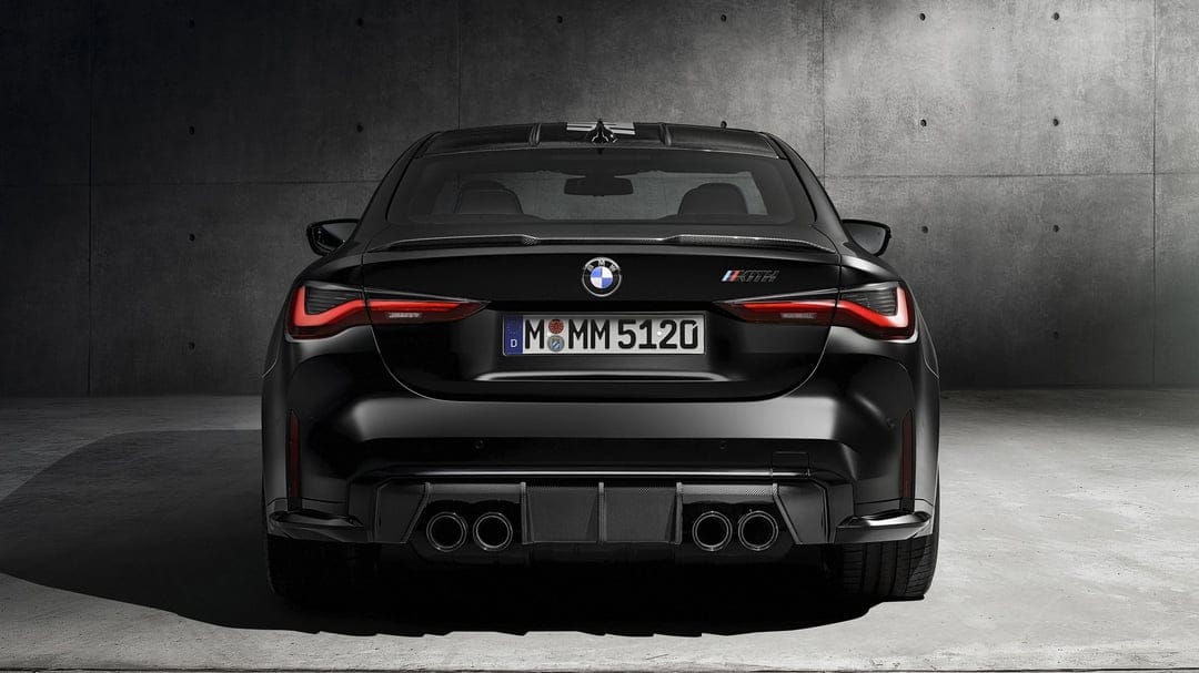 Rear view of a black BMW M4 Kith with glowing red taillights and quad exhausts against a concrete wall.