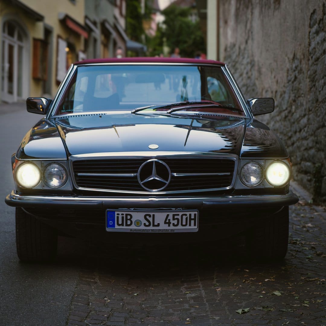 Black Mercedes-Benz SL 450 convertible with a burgundy top parked on a cobblestone European street at night.