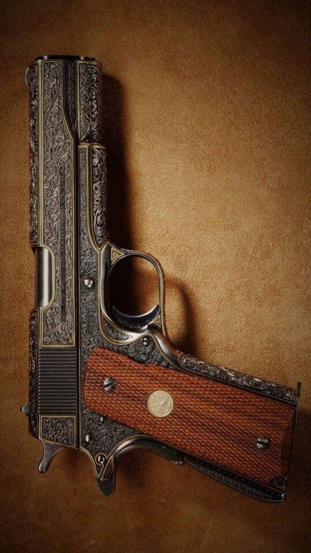 Colt 1911 pistol with ornate floral scrollwork, gold inlays, and textured wood grips on a brown background.